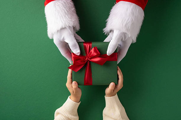 istock Christmas gift exchange featuring Santa handing a wrapped present to a child's hands 2231879835