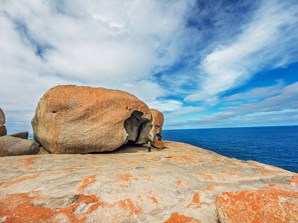 A tourist takes in the views of the abstract and remarkable granite rock formations. The uniquely shaped boulders are coated with orange lichen.  The rocks are located in Flinders Chase National Park, (Kangaroo Island) Australia.  The ocean to the left is the Great Australian Bight.