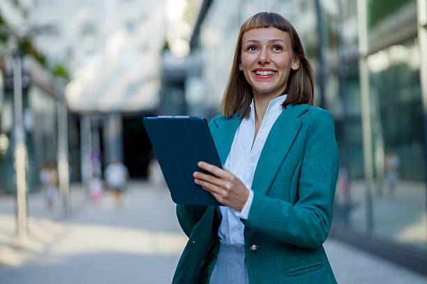 istock Young businesswoman smiling while using a digital tablet in an urban setting, glancing away with a confident expression 2231893214