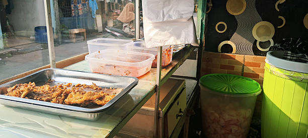 A food cart displaying fried snacks on a tray, plastic containers, and a large jar filled with crackers under afternoon sunlight.