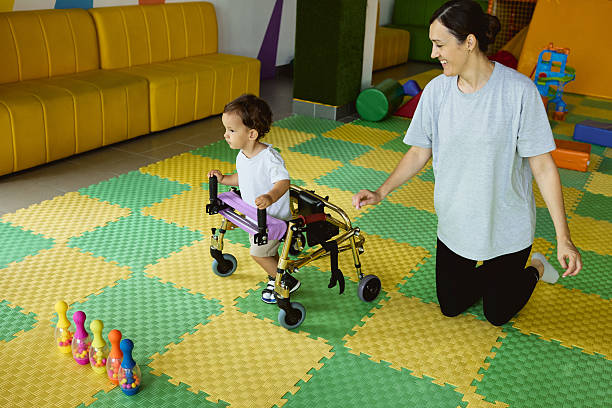 istock Physical therapist assists a young boy with movement disorders as he engages in physical rehabilitation using a walker in therapy room 2231901504