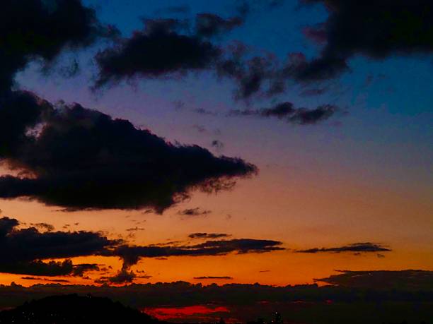 A bright orange, pink and blue sky during Sunset with Cumulonimbus Clouds in front, which are storm clouds across Auckland's Harbor. This was taken from Bastion Point at Auckland's Waterfront.