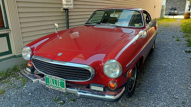 Bennington, Vermont - August 21, 2025: Red 1970s Volvo 1800E Coupe, parked in a gravel-covered driveway