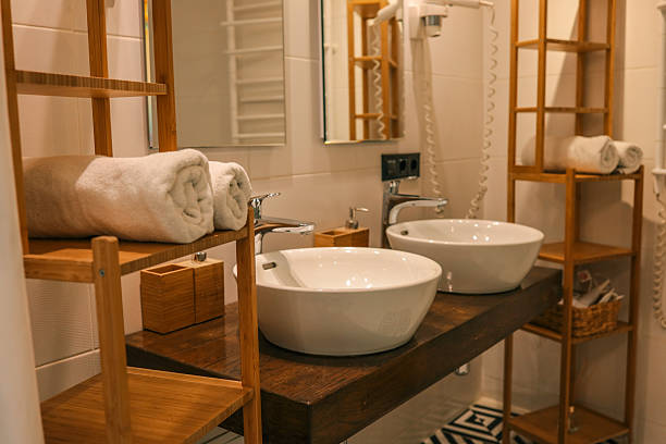 istock Modern bathroom interior with double white ceramic sinks, wooden shelves, and rolled towels, featuring patterned tiles and warm lighting 2231918379