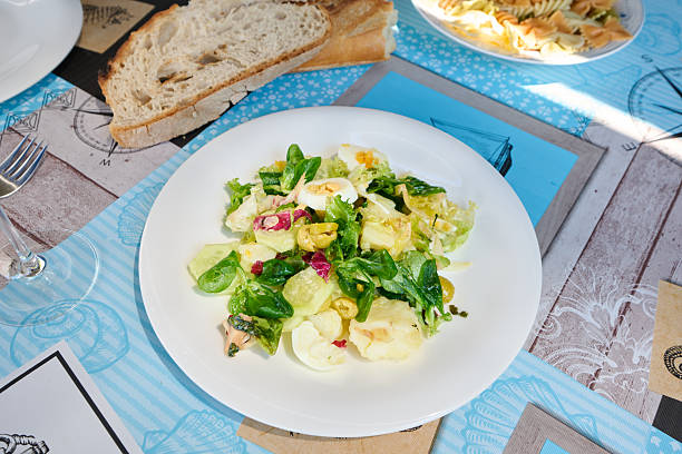 Vibrant mixed salad with boiled eggs, cucumber, olives, and lettuce, served on a plate with nautical themed placemat, accompanied by bread and pasta