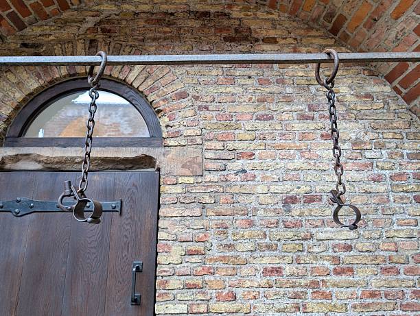 Old iron shackles and chains are mounted on a rustic brick wall, showcasing a piece of history. The display provides insights into past practices of restraint.