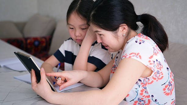 The tutor teaches the child. Home schooling. Mom explains a difficult math topic to her daughter. A woman and a child do their homework using a tablet