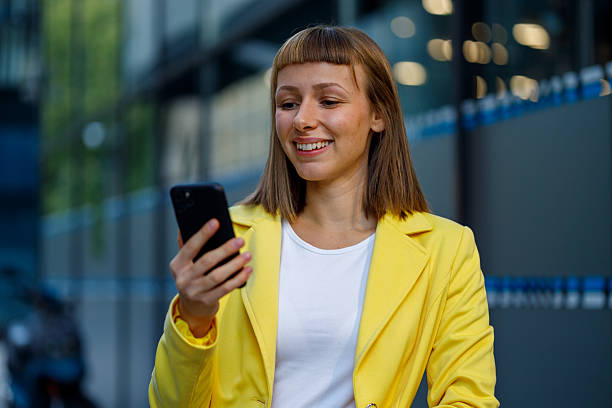 istock Professional woman networking on smartphone, walking downtown wearing bright yellow jacket 2231938417