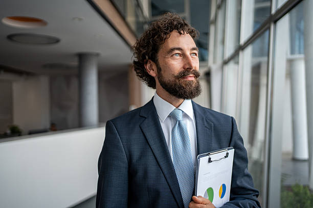 istock Businessman holding clipboard looking out office window 2231941282