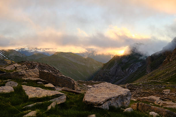 Sunset in the mountains, rays of sunlight filter through the clouds that obscure the peaks.