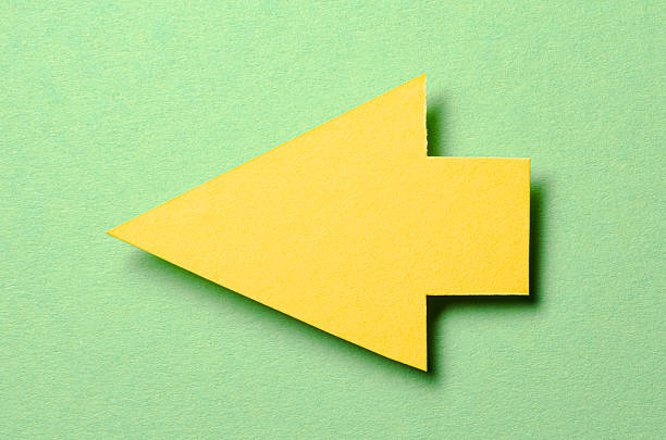 Yellow cut out blank paper cardboard arrow direction sign with copy space for text on green background, flat lay top view pointing symbol message backdrop