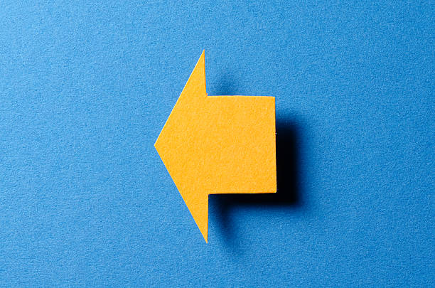 istock Orange blank paper cardboard arrow direction sign with shadow and copy space for text on blue background, flat lay top view pointing symbol message backdrop 2231942639
