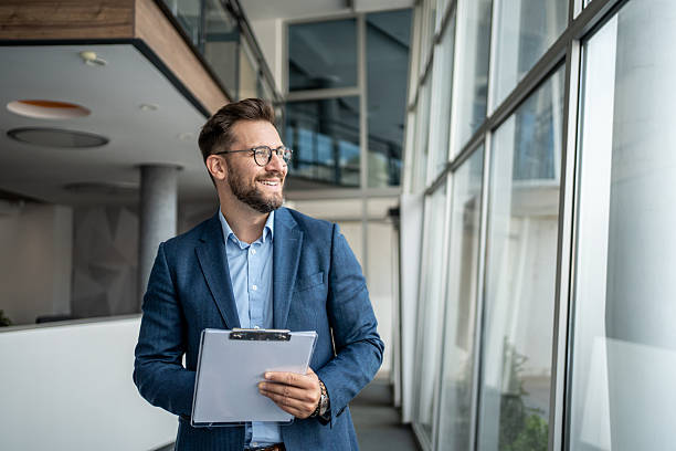 istock Businessman smiling and holding clipboard in modern office 2231949188