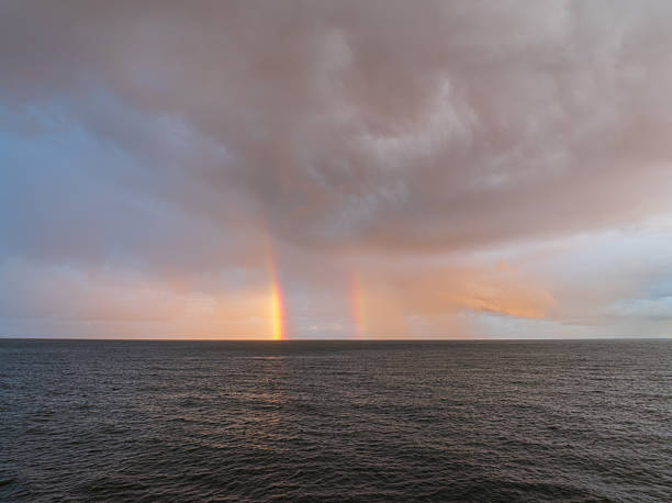 A spectacular double rainbow emerges from dramatic sunset clouds above the serene and vast waters of the Baltic Sea.High quality photo