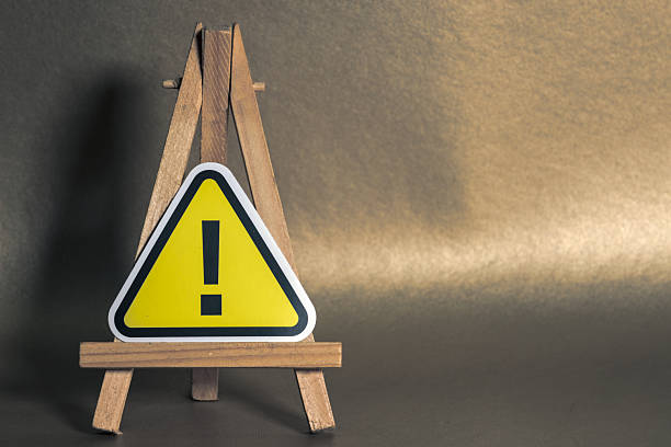 Yellow warning sign with exclamation mark on wooden easel, set against a brown gradient background, symbolizing caution and alert.