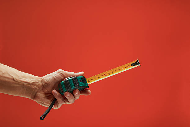 Hand holding a tape measure extended against a vibrant red backdrop, ideal for construction or diy themes
