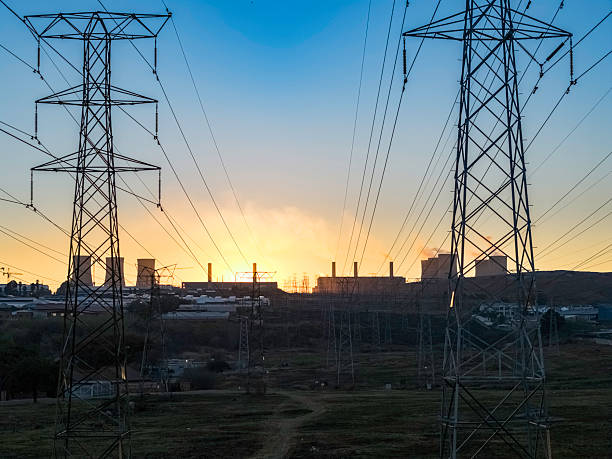 Pylons holding high voltage electrical cables seen at sunrise with a power station in the distance.