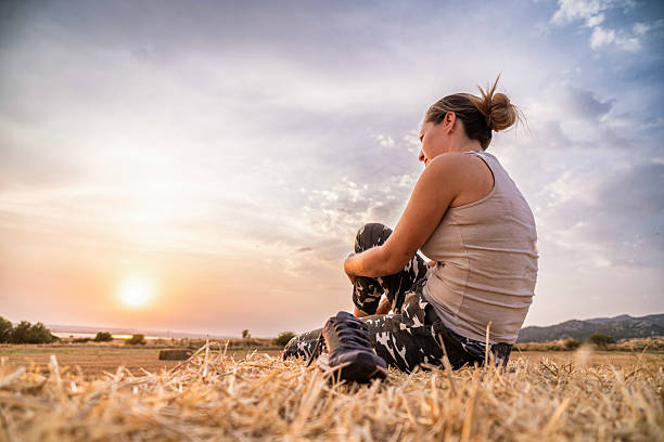 Female farmer relaxing on hay bale, enjoying a serene sunset view in the countryside