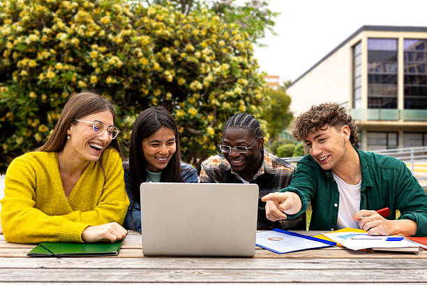 istock University students collaborating on a project outdoors, sharing a laptop and smiling 2231966724
