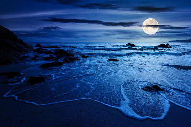 istock calm sea landscape with wave rolling on sandy beach with boulders at night 2231968357