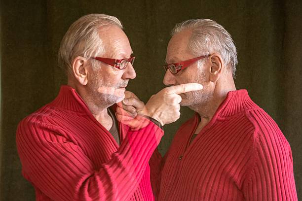 An elderly man as a digital twin points the finger at himself and looks into his own eyes.