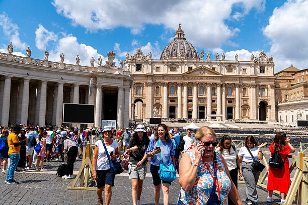 Rome - Lazio - Italy - 08-02-2025: A large group of people walks across the square in front of the St. Peters Basilicafacade with columns, statues and dome under a partly cloudy sky.