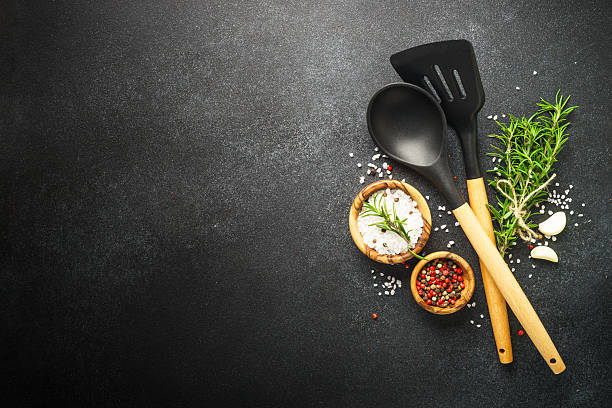 istock Kitchen table with utensils, herbs and spices on black. 2231982268