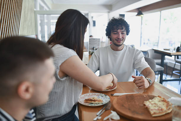 istock Female Putting Pizza Slice To Plate While Enjoying Lunch Break With Friends 2231984257
