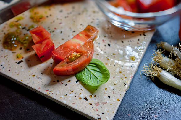 Fresh heirloom tomatoes are being chopped on a cutting board in a bright kitchen. The ingredients are ready for a delicious ratatouille - food and drink, preparing food