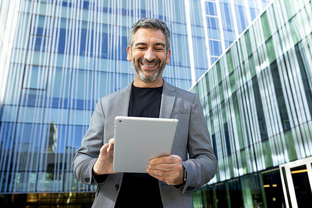 istock Smiling businessman using digital tablet in front of office building 2231986143