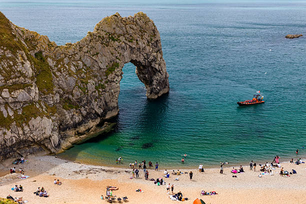 Holidaymakers swimming and relaxing on the beach by the iconic Durdle Door rock arch.