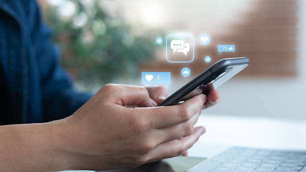 istock Hand using a smartphone with hologram social media icons including likes, comments, and notifications, symbolizing digital marketing, online communication, mobile engagement, and social networking. 2231991648