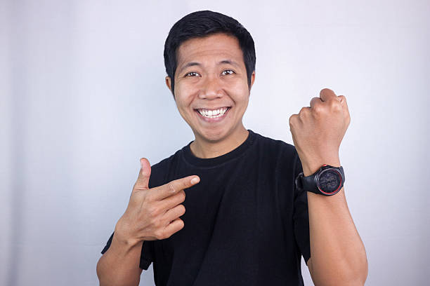 istock Smiling asian man pointing his watch, looking at camera. isolated on white background 2231992009