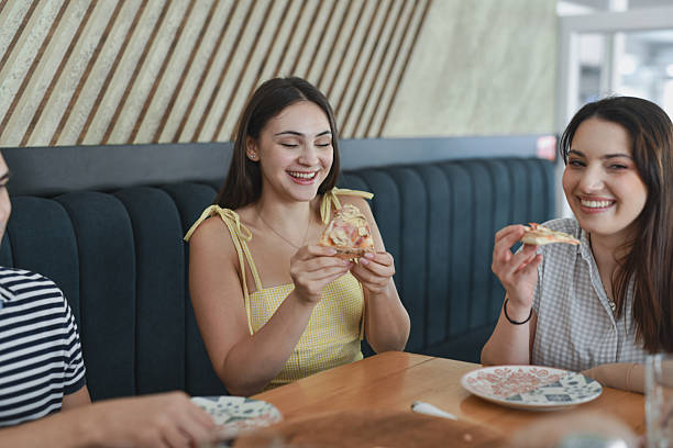 istock Group Of Smiling Friends Gathered Around Table Enjoying Pizza 2231996488