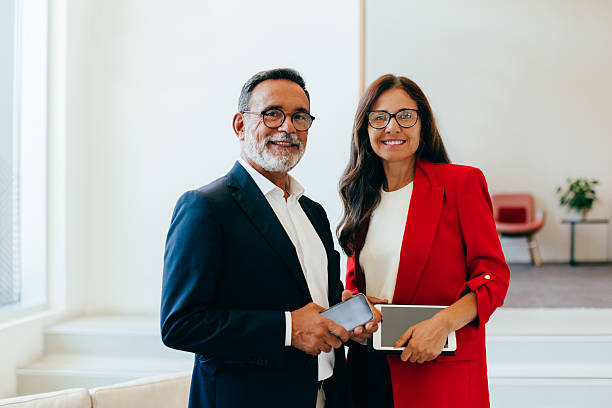 istock Smiling senior business professionals posing in formal attire holding tech devices 2231996787