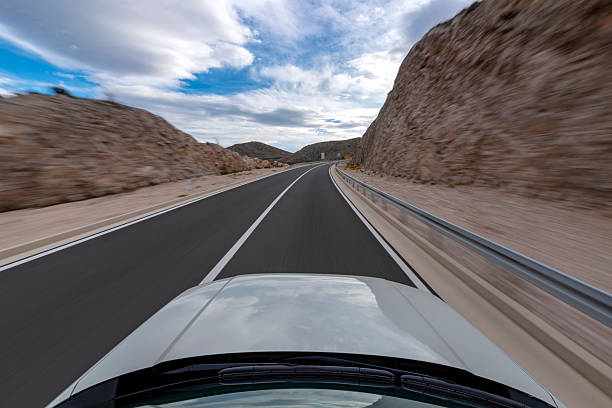 Blurred action from a car at high speed, showing a spinning wheel and a metal fence next to the road