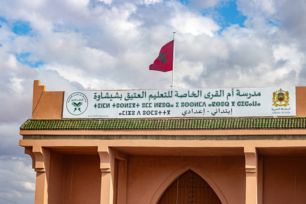 The building in the photo is the Umm al-Qura Private School for Traditional Education (Madrasat Umm al-Qura al-Khasa li-Ta’lim al-‘Atiq), located in Chichaoua, Morocco, a provincial town about 70 km west of Marrakesh. The school operates under the supervision of the Moroccan Ministry of Endowments and Islamic Affairs, which oversees institutions dedicated to traditional Qur’anic and Islamic studies. The sign at the entrance, written in Arabic, Tifinagh (the Amazigh script), and French-style numbering, indicates that the school offers primary and preparatory-level education. The green-tiled roof is a typical feature of Moroccan architecture, often used on religious and educational institutions. Above the sign flies the Moroccan national flag, red with a green five-pointed star, symbolizing sovereignty, unity, and Islam.
