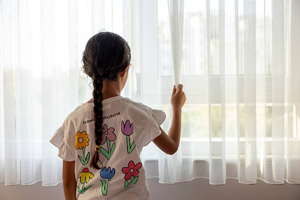 Little girl pulling back the curtain to let sunlight into the room