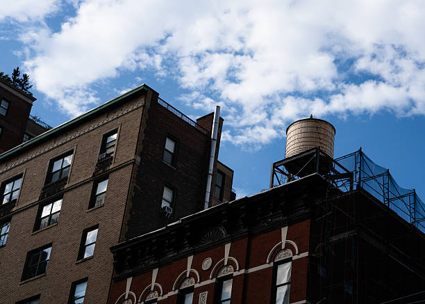 A brick building with a water tower on top. The sky is blue with some clouds. The building is old and has a lot of windows