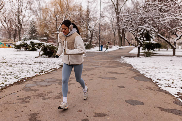 Active young woman warming up with a stretch before jogging in a snowy park on a cold winter day.