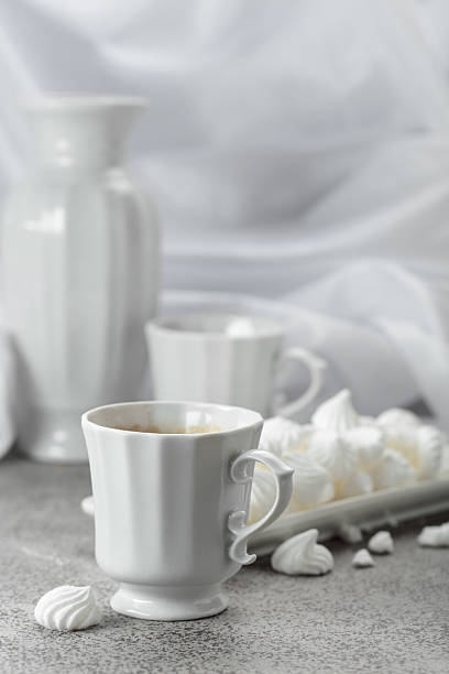 Black coffee in white porcelain cup and white small French meringues.