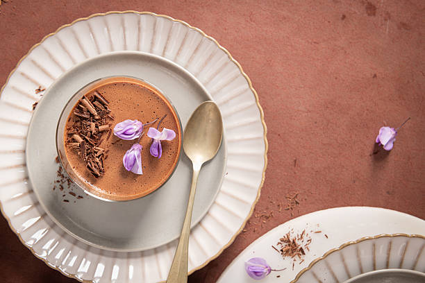 istock An overhead view captures a single creamy chocolate mousse in a glass, styled on plates with a spoon, chocolate shavings, and purple flowers. 2232042844