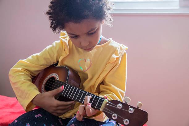 istock Multiethnic child plays a small guitar indoors while sitting on a bed during the day 2232046401