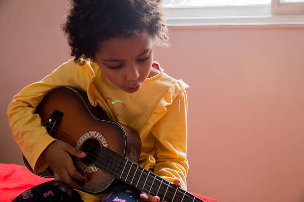 istock Young girl playing ukulele indoors during afternoon sunlight 2232046452