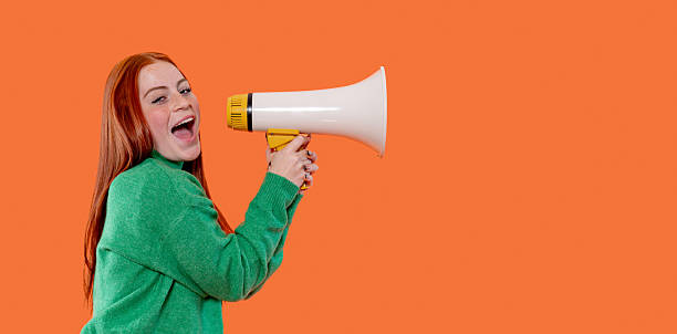 istock Young woman energetically shouting into a megaphone against a bright orange background during a spirited event or campaign 2232051099