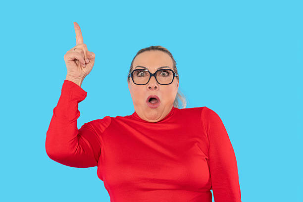 istock Surprised woman with glasses raising finger against bright blue background while wearing a red top 2232053708