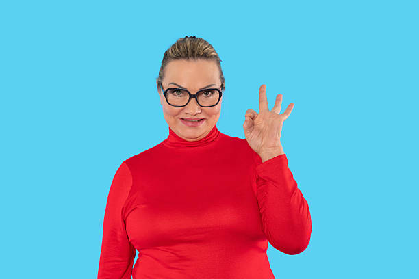 istock Confident woman in red sweater making hand gesture against blue background, expressing positivity and assurance in a vibrant setting 2232053740