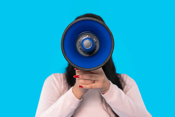 Woman holding a blue megaphone against a bright blue background while preparing to address an audience