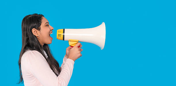 istock Woman enthusiastically using a megaphone in front of a bright blue background during a lively event, conveying her message with energy and passion 2232055823