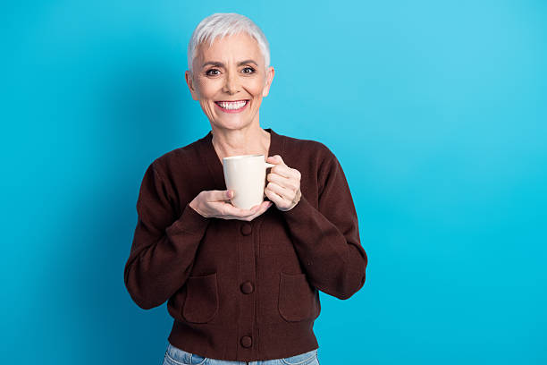 istock Happy elderly woman holding cup while smiling confidently against vibrant blue background 2232056909